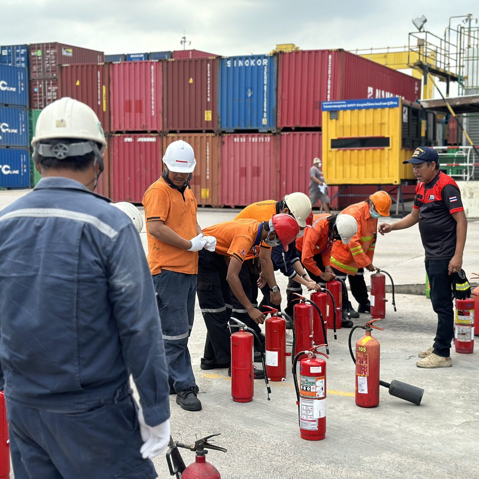 Workers practicing fire extinguisher use at a shipping yard.