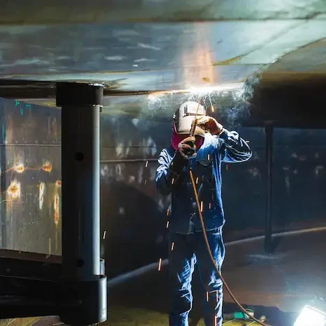 A worker in protective gear welding metal indoors.