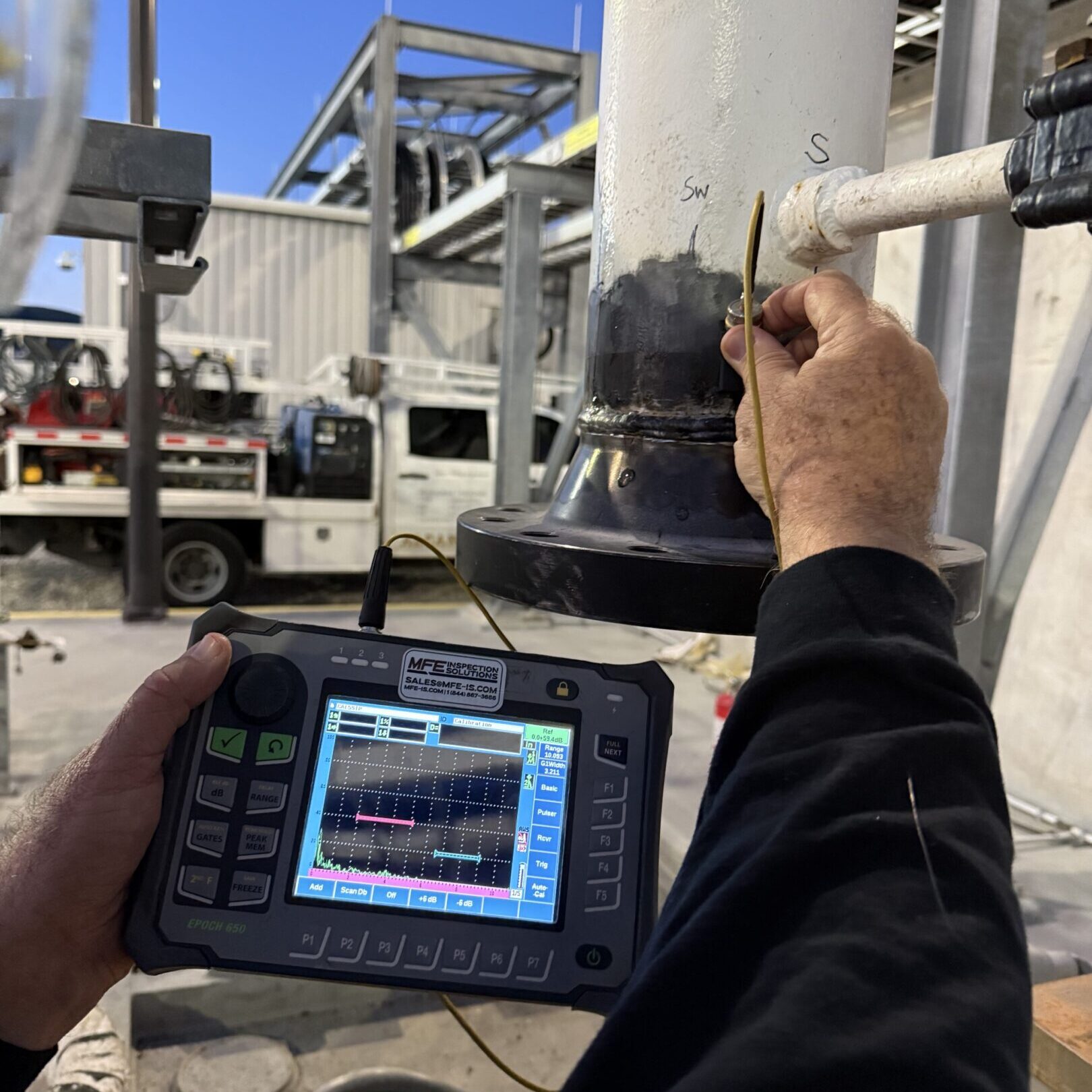 Technician uses handheld device to inspect industrial equipment outdoors.